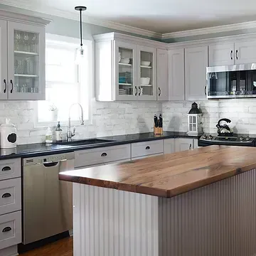 A kitchen with white cabinets , stainless steel appliances , a wooden counter top and a large island.
