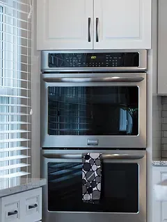 A stainless steel double oven is sitting in a kitchen next to a window.