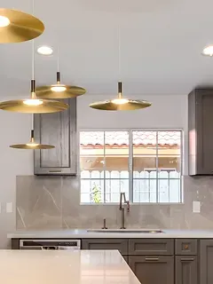 A kitchen with a sink , cabinets , and pendant lights hanging from the ceiling.