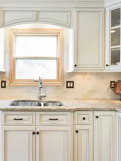 A kitchen with white cabinets , granite counter tops , a sink and a window.