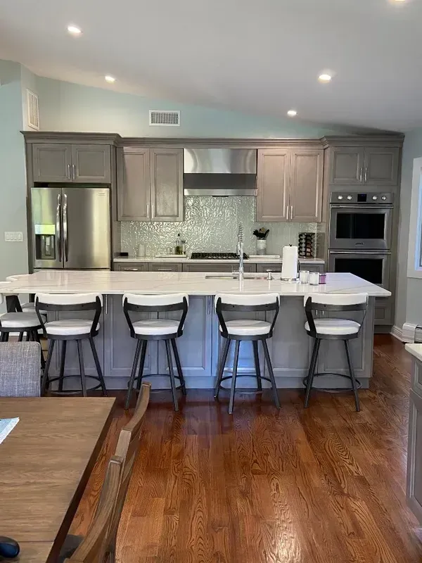 A kitchen with a large island , stools , a table and a refrigerator.