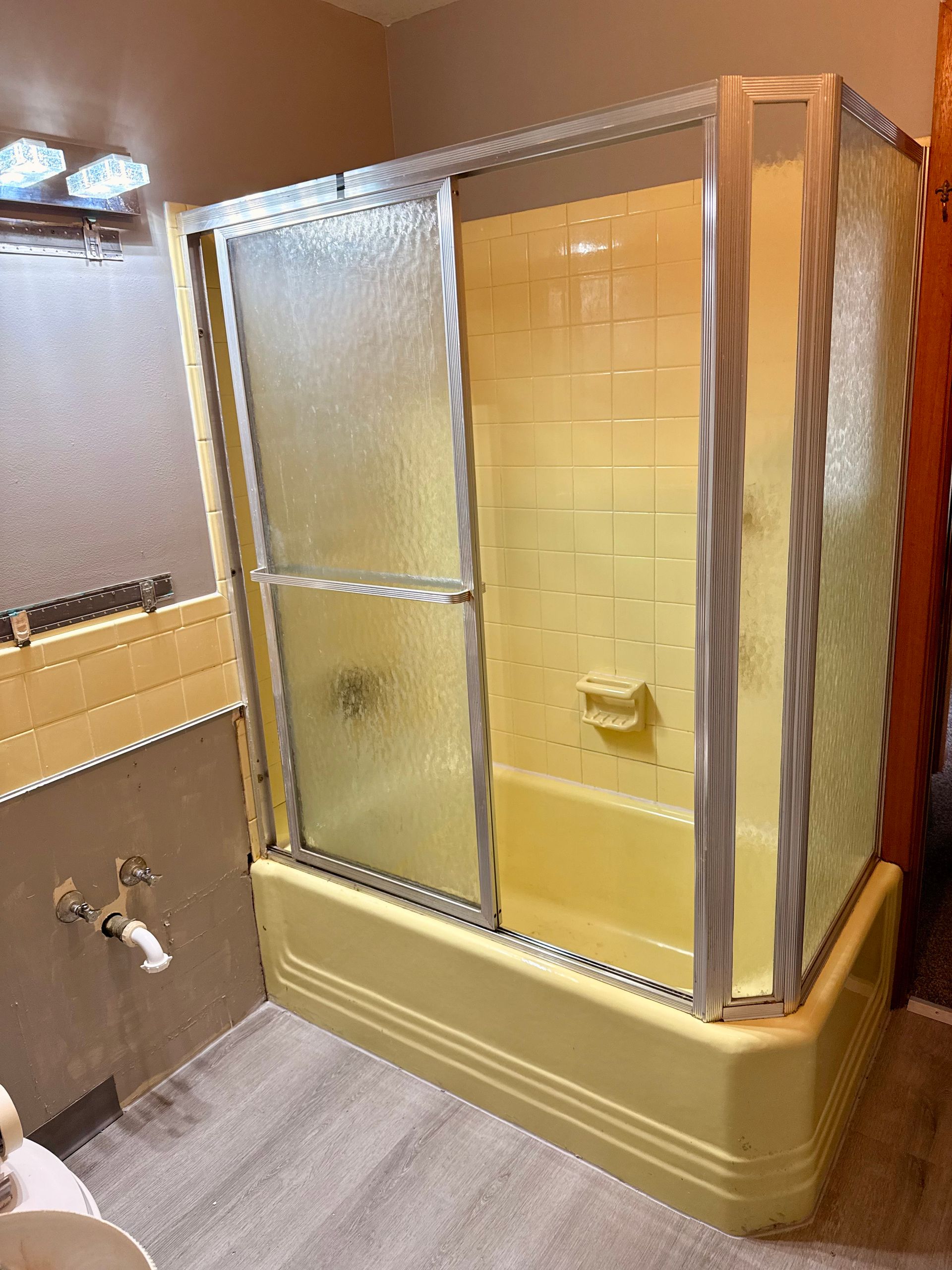 Picture of a tub and shower that is outdated and needs refinishing. You can see a yellow tub and shower.