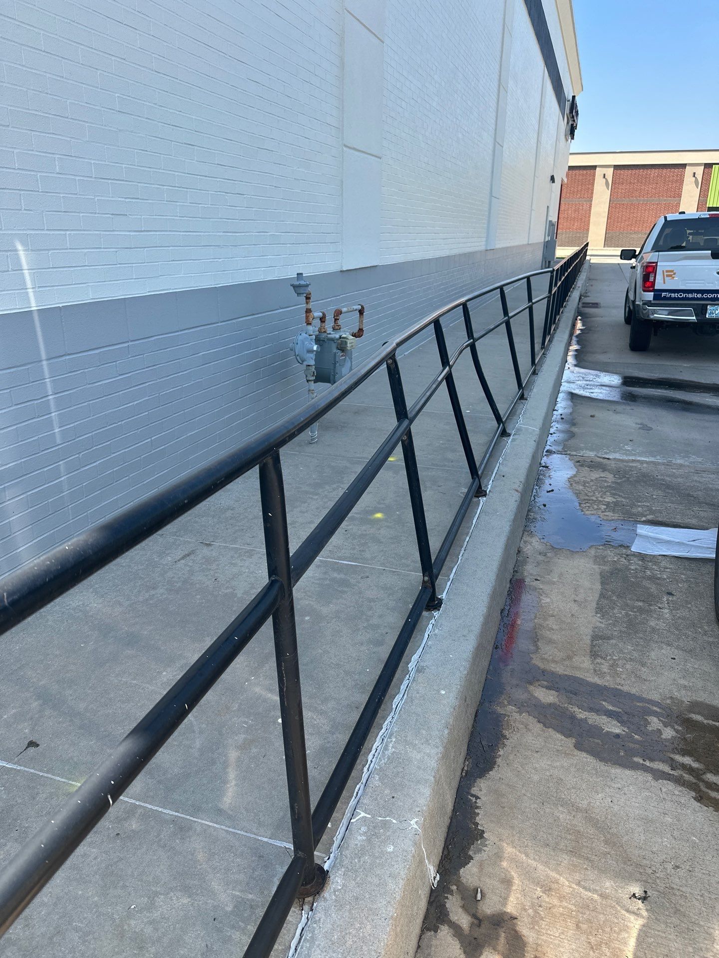 A black railing is along the side of a building next to a parking lot.