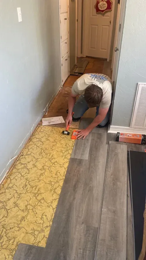 A man is installing a vinyl floor in a hallway.