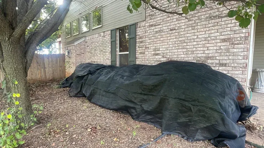 A large black tarp is sitting in front of a brick house.