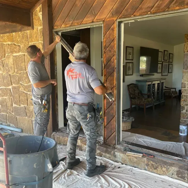 Two men are working on a sliding glass door in a house