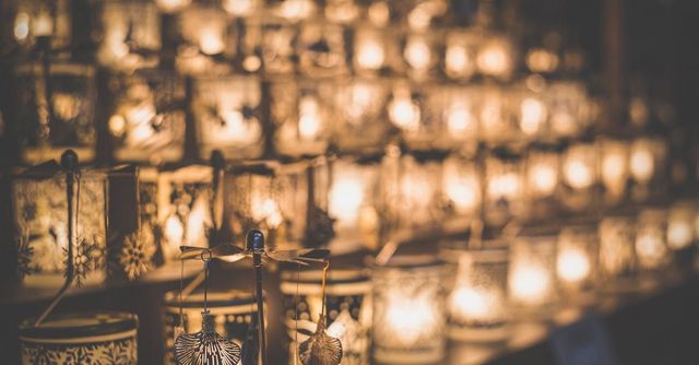 Rows of warm glowing candles and lanterns filling a dim, reflective space