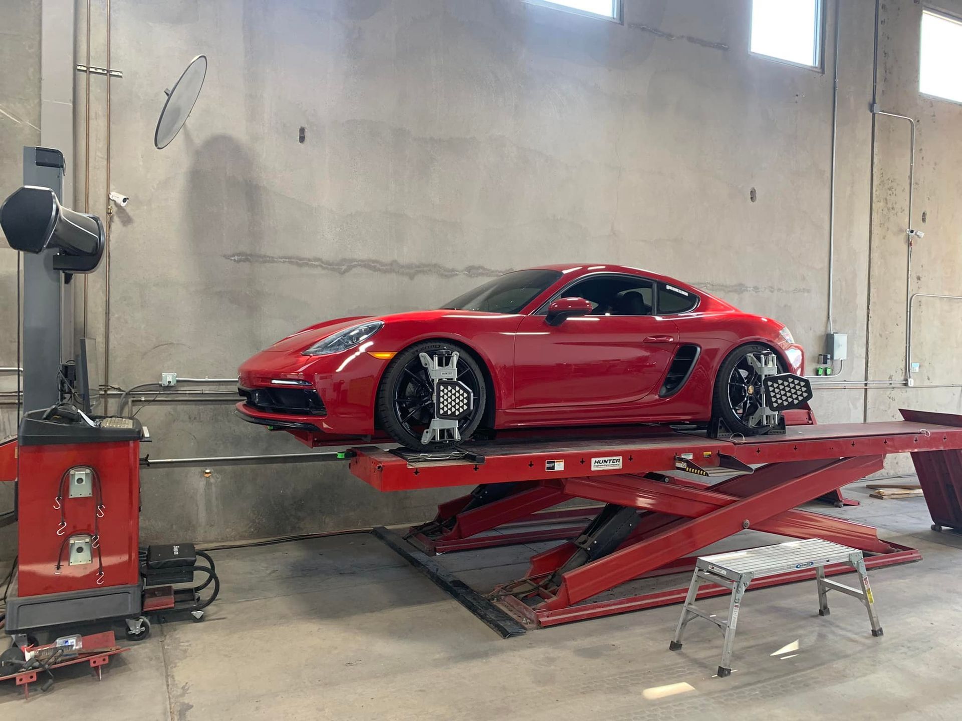 Red sports car on a red lift in a garage, undergoing wheel alignment.