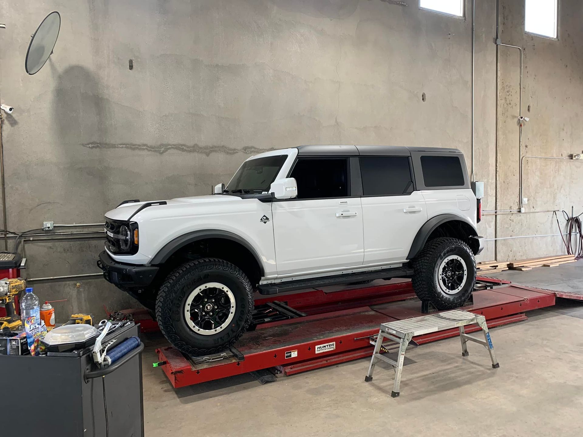 White Ford Bronco on a red lift inside a garage.