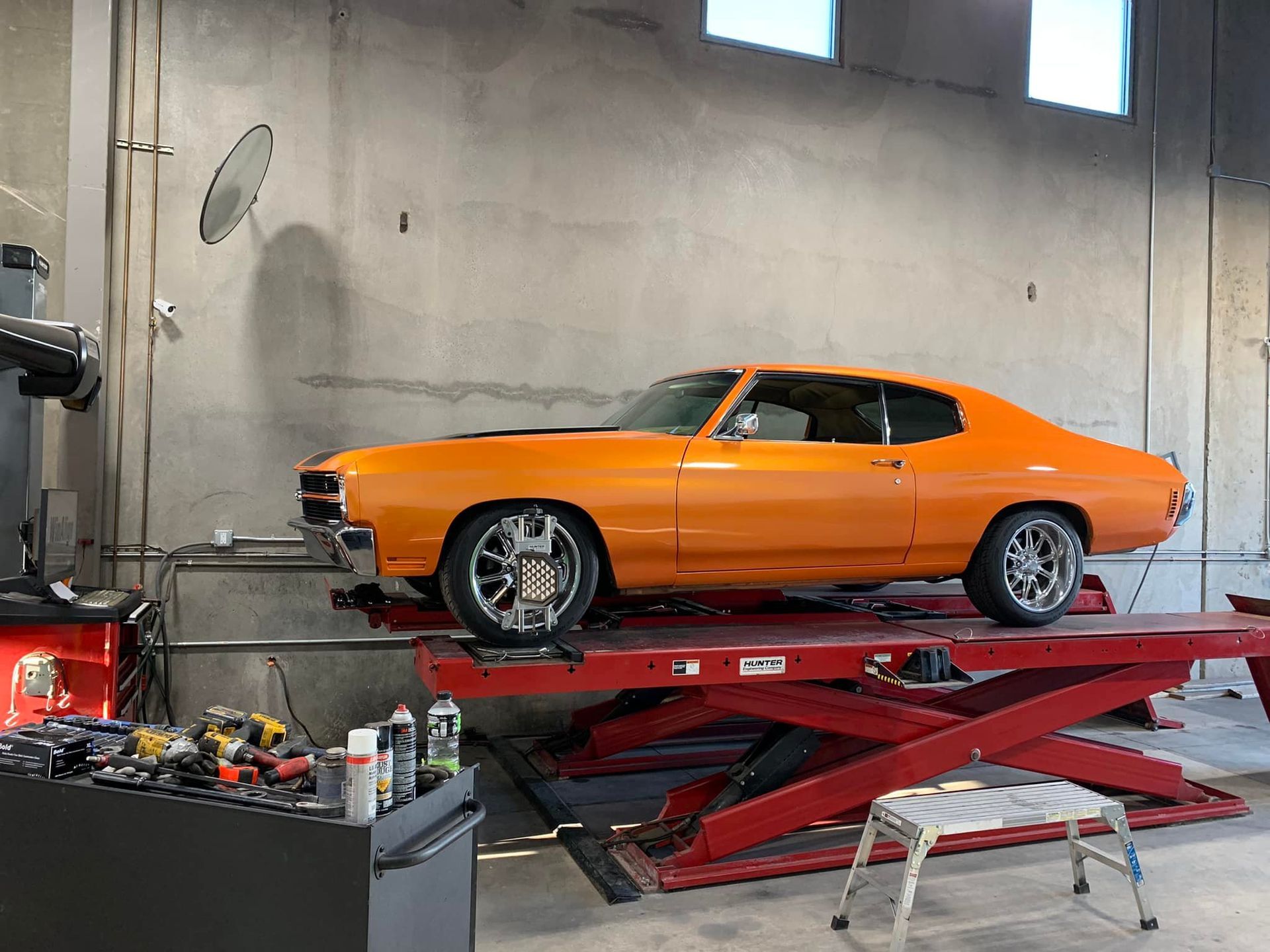 Orange classic car on a red lift in a garage, undergoing work.