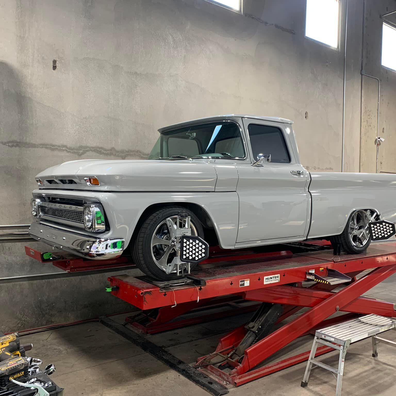 Gray vintage pickup truck on a red lift for wheel alignment in a garage.