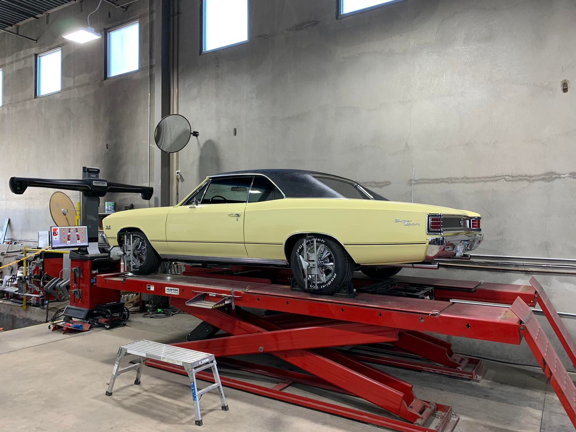 Yellow classic car on a red lift in a garage, undergoing alignment.
