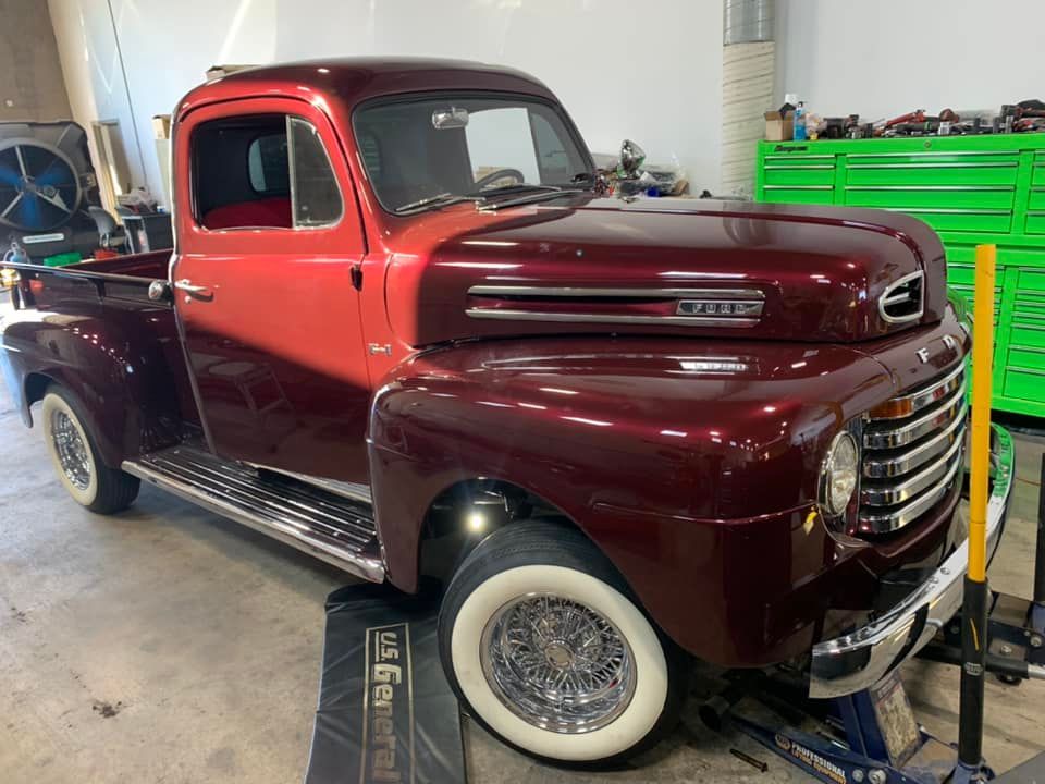 Two-tone burgundy vintage Ford pickup truck with white wall tires, in a shop.