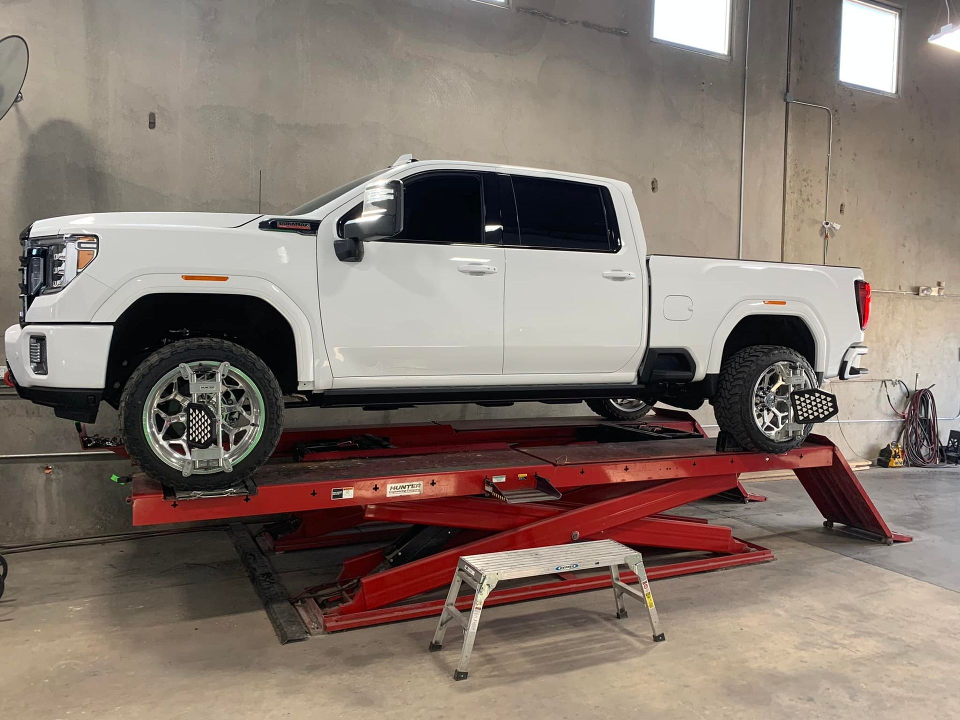 White pickup truck on a red hydraulic lift inside a garage.