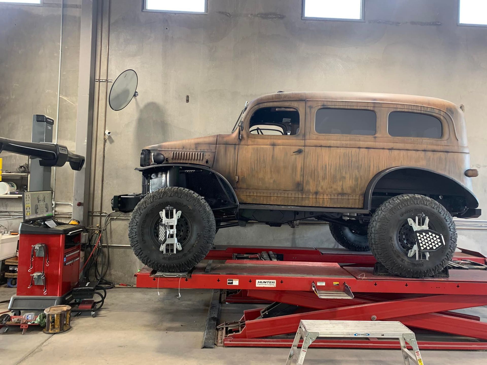 Brown, lifted, vintage SUV on a red lift inside a garage, undergoing an alignment.