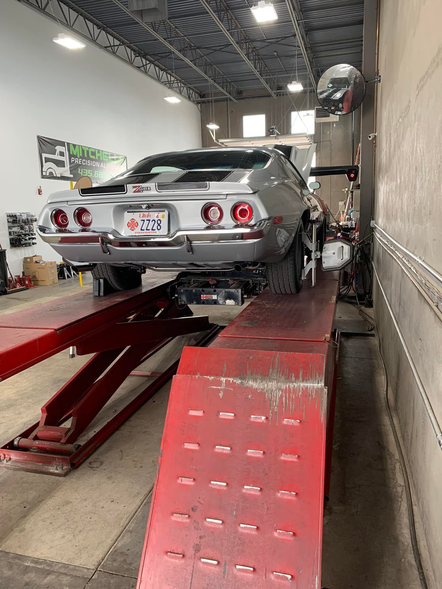Silver classic car on a red hydraulic lift inside a garage.