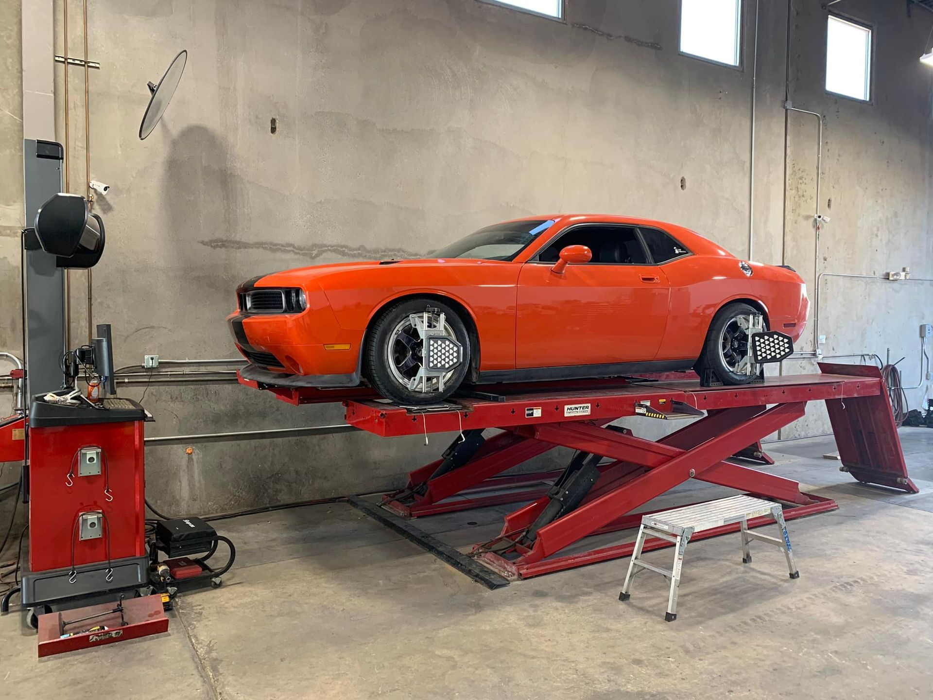 Orange Dodge Challenger on a red car lift in a garage, undergoing wheel alignment.