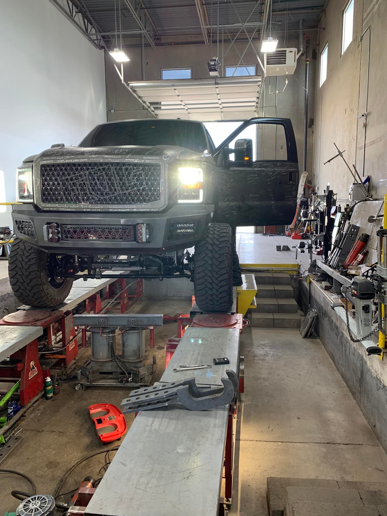 Black lifted truck on a lift inside a repair shop. Door open.
