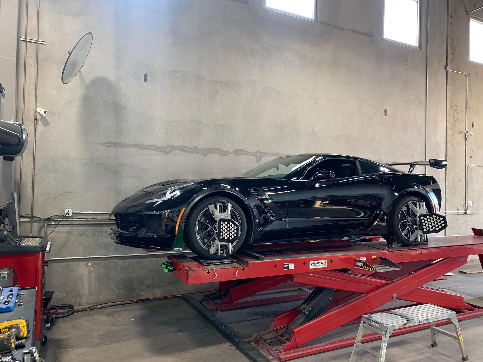 Black sports car on a red lift in a garage, undergoing wheel alignment.