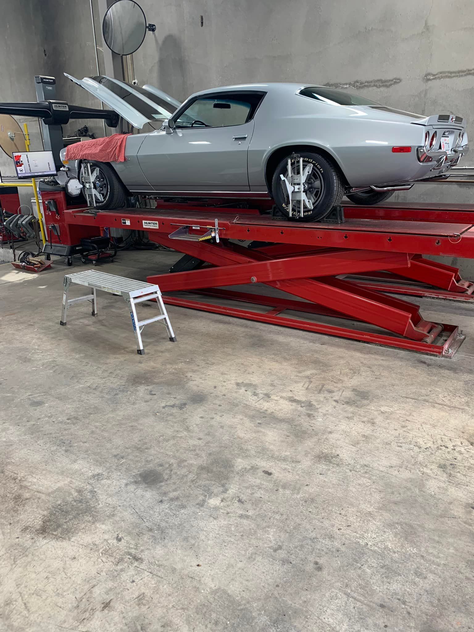 Silver classic car on a red lift in a garage, undergoing wheel alignment.