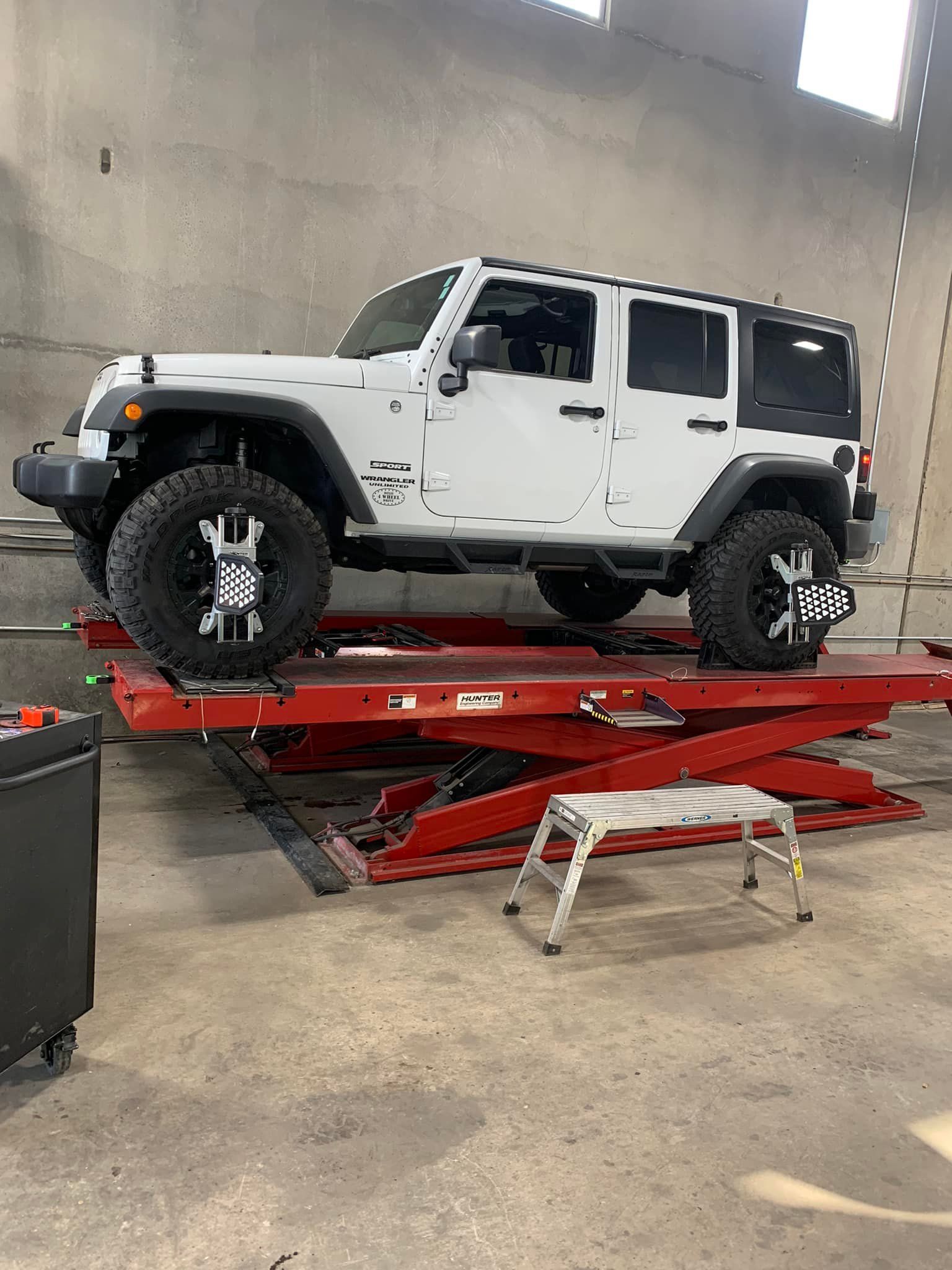 White Jeep Wrangler on a red lift inside a garage.