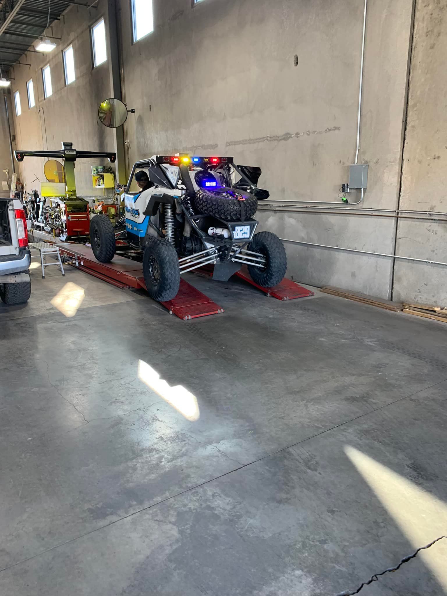 Off-road vehicle on red ramps inside a concrete building with emergency lights on.