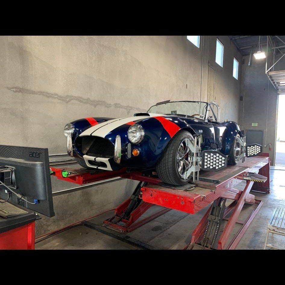 A dark blue sports car with white and red stripes on a lift in a garage.