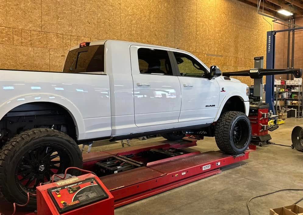White pickup truck on a red lift in a garage, undergoing an alignment check.