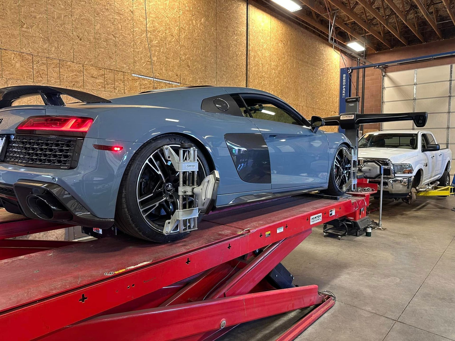 Gray Audi R8 sports car on a red lift undergoing wheel alignment in an auto shop.
