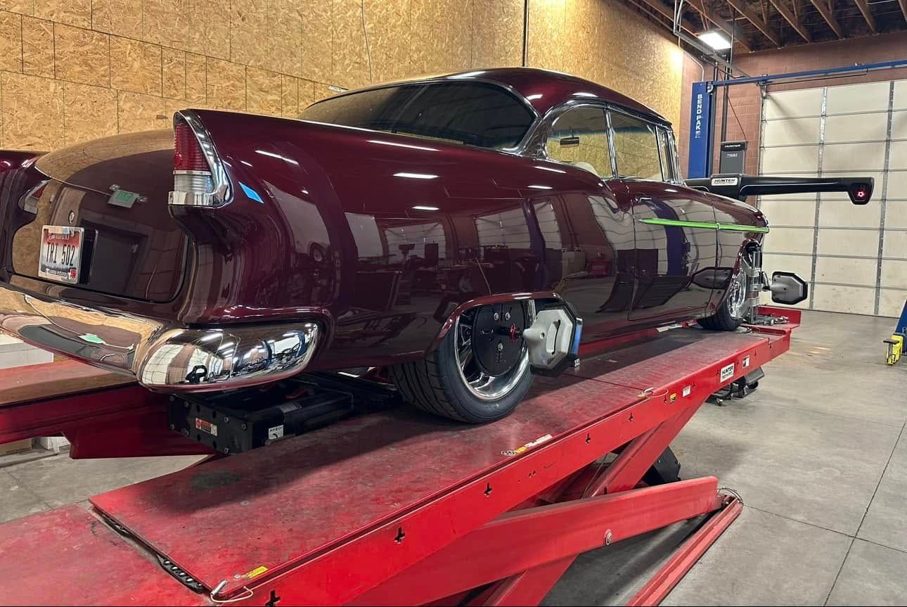 Maroon classic car on a red lift inside a garage.