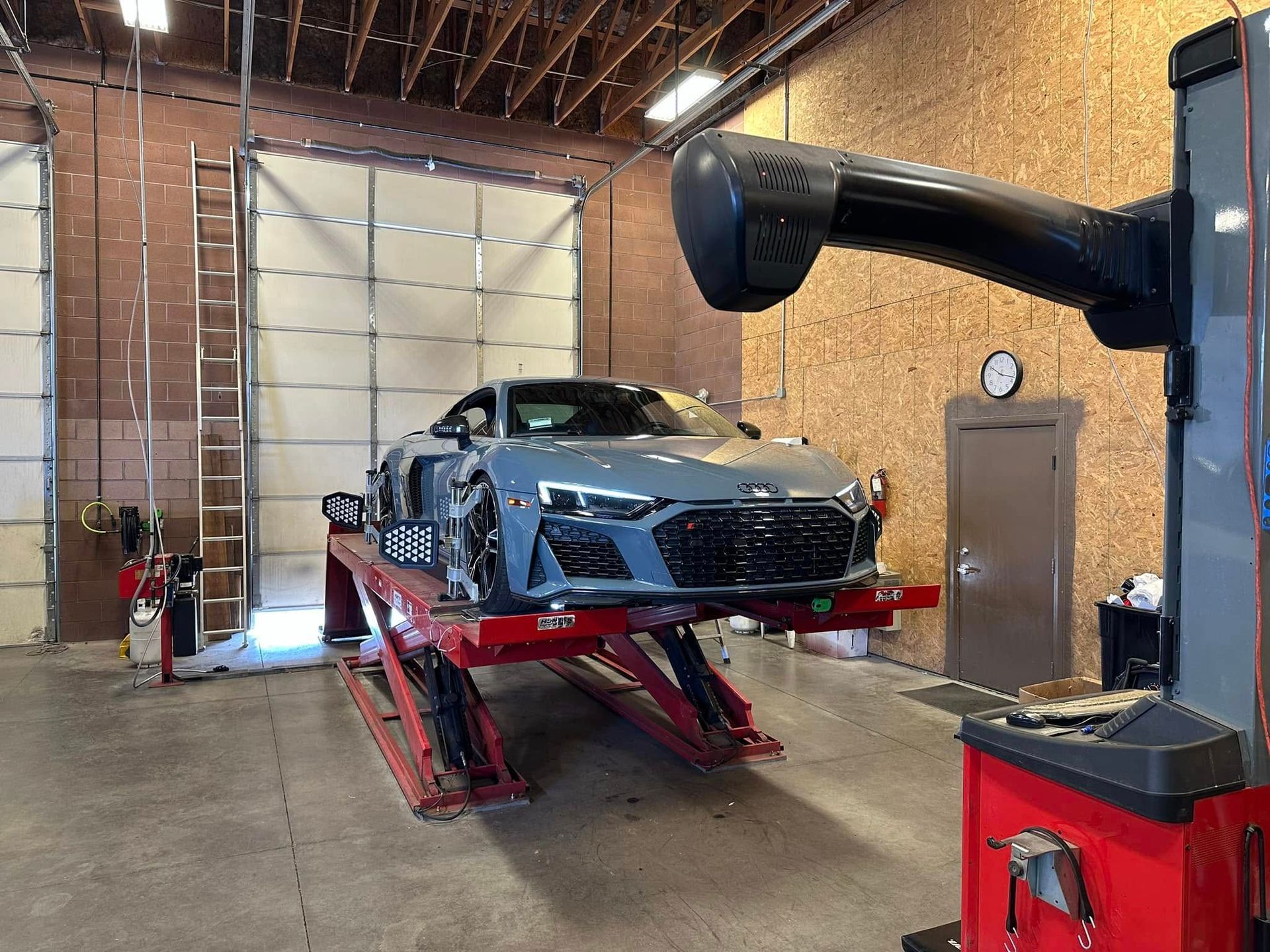 Gray Audi R8 on a red lift in an auto repair shop with alignment equipment.