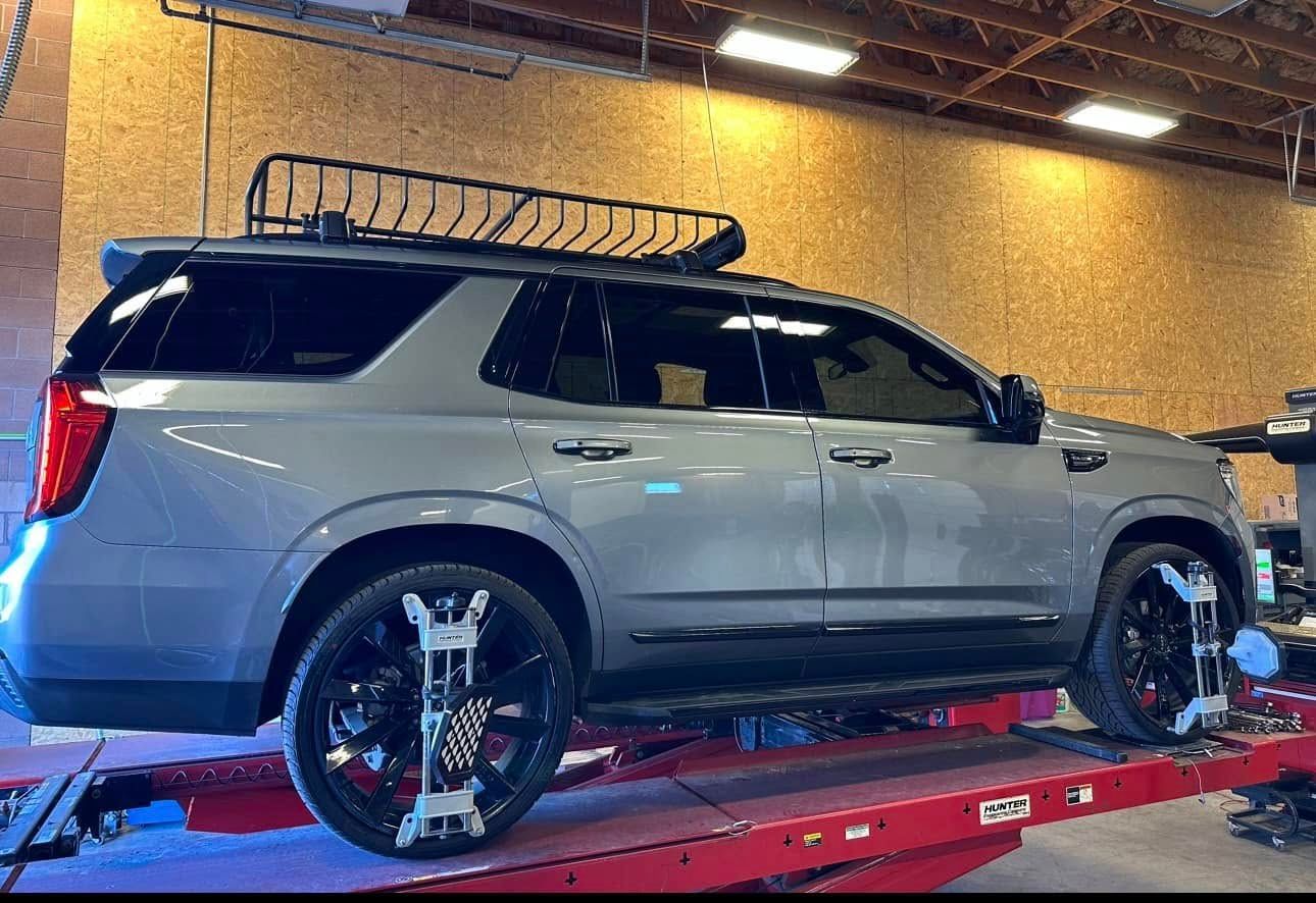 Gray SUV on a car lift; alignment equipment attached to wheels. A roof rack is visible.