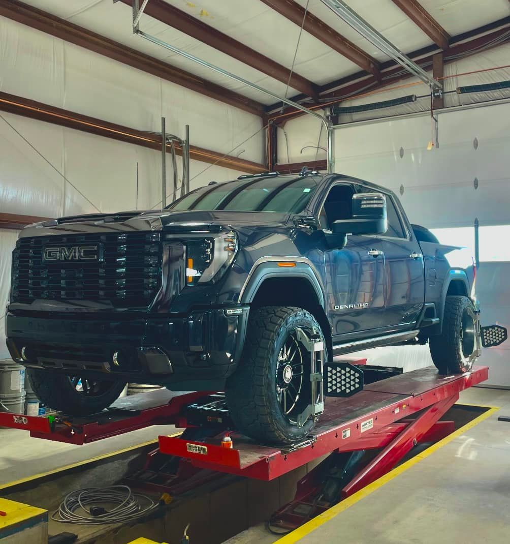 Dark blue GMC pickup truck on a red lift in a repair shop.