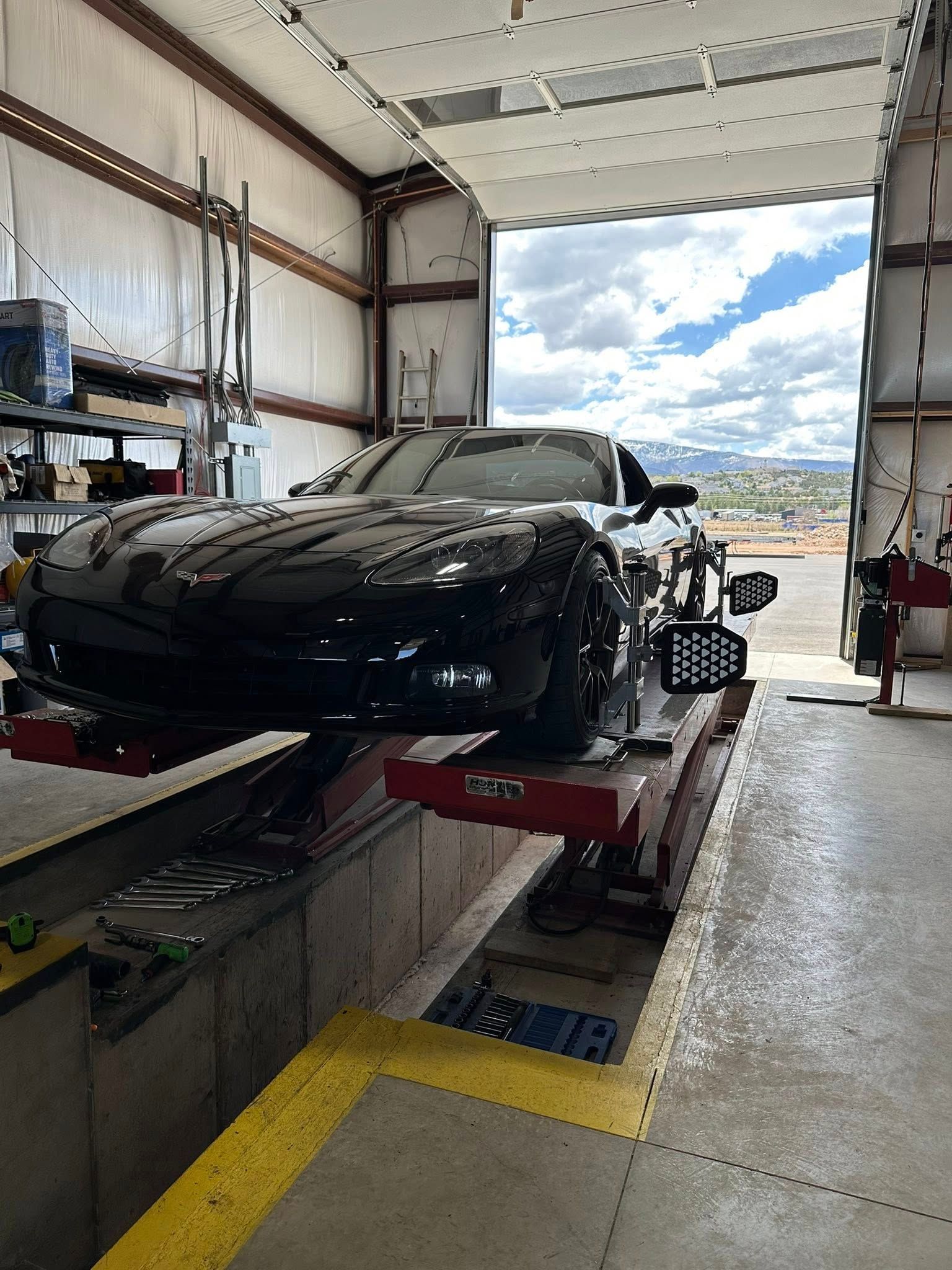 Black sports car on a lift in a garage, undergoing alignment.