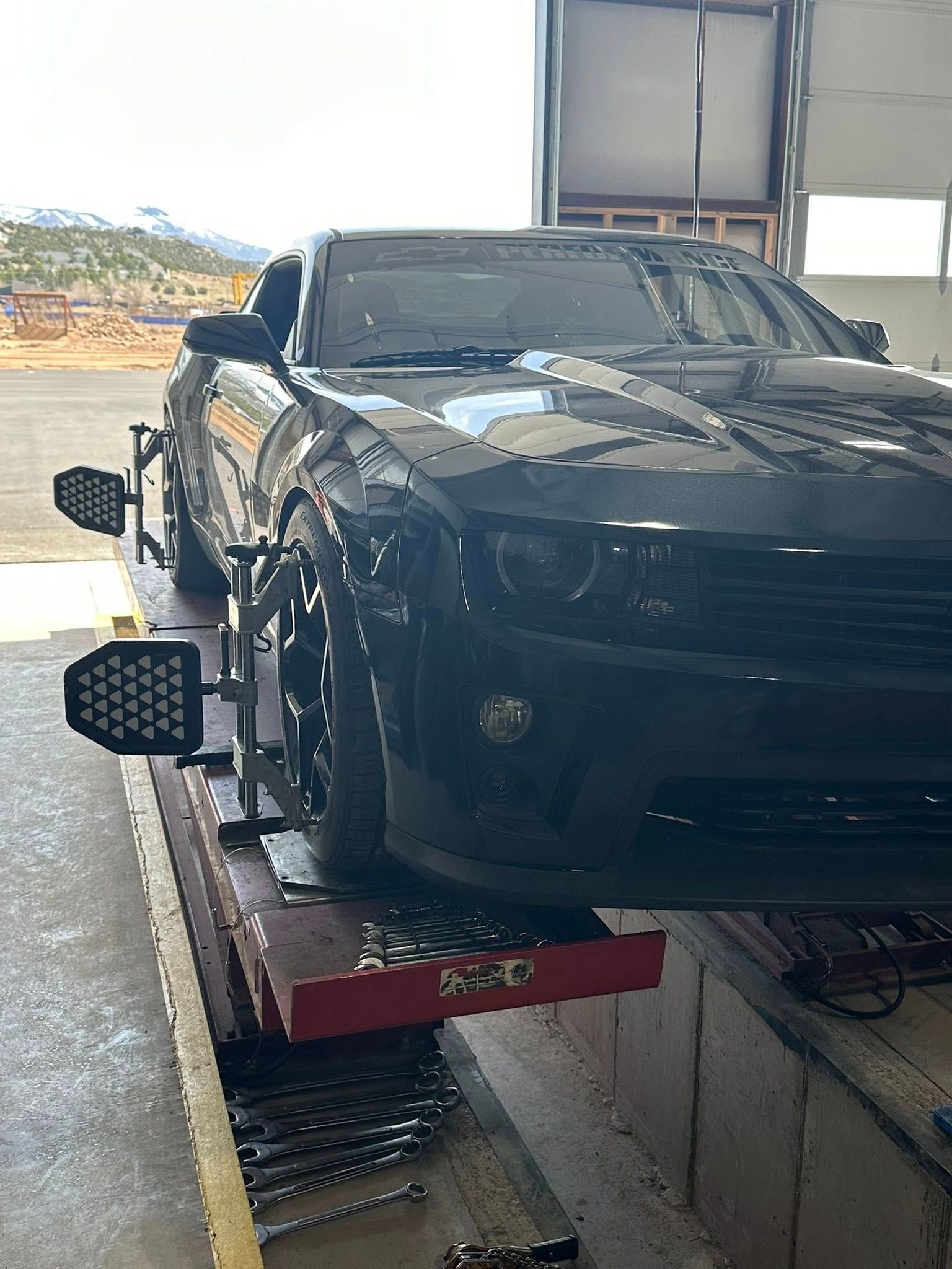 Black car on a lift with alignment tools attached, inside a garage.