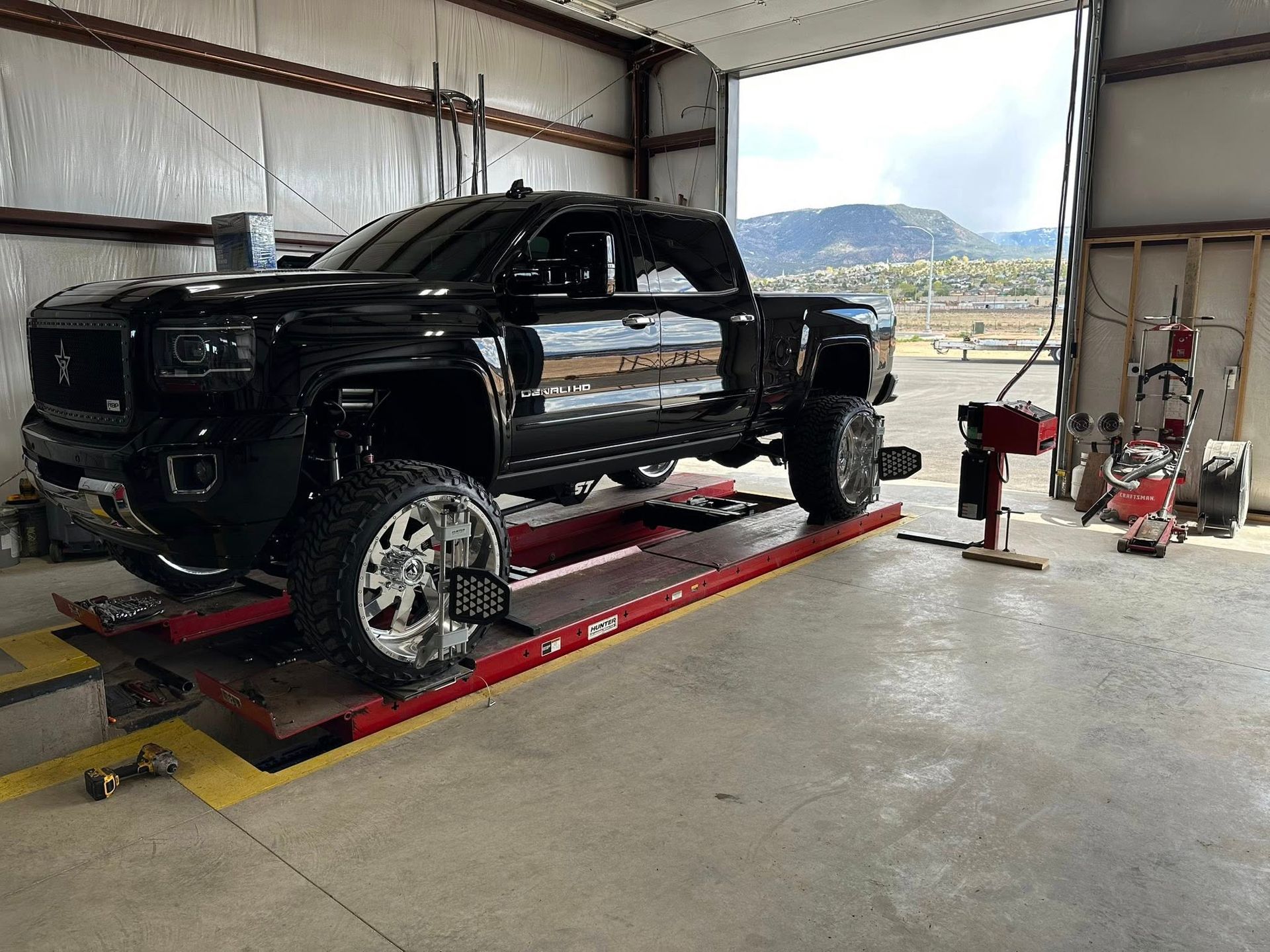Black lifted truck on alignment rack in garage with mountain view.