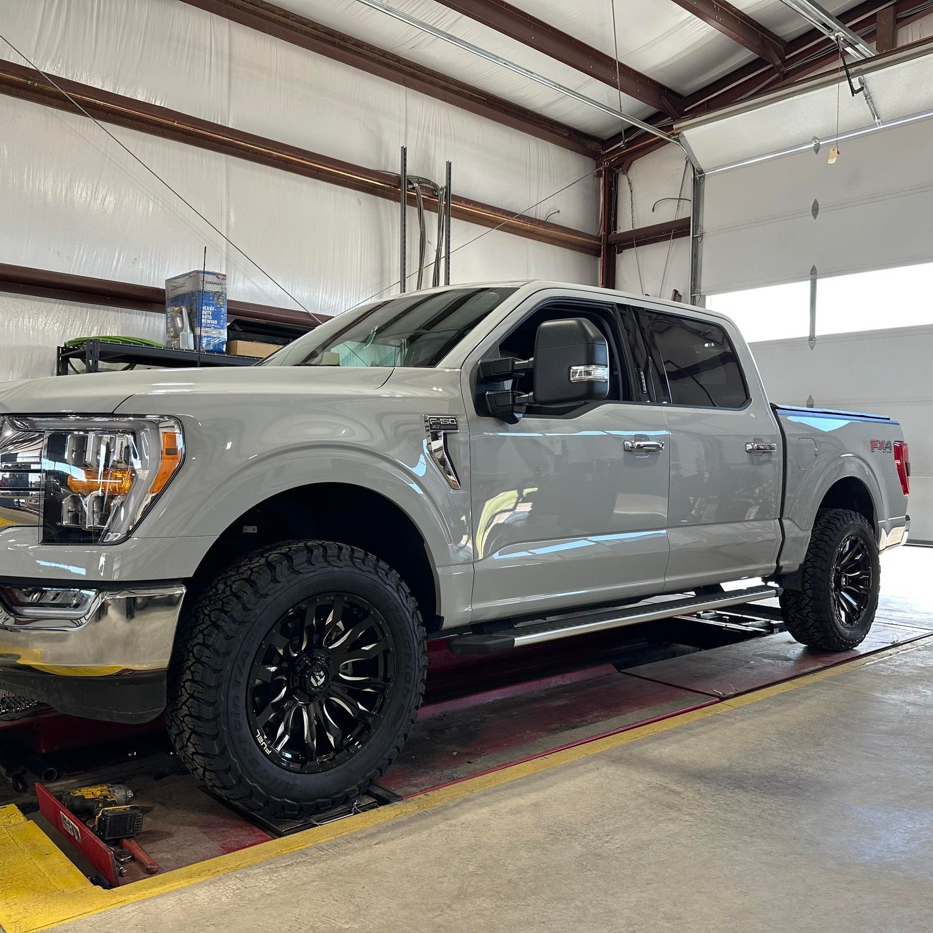 Gray Ford pickup truck inside a garage, with black wheels, on a lift.