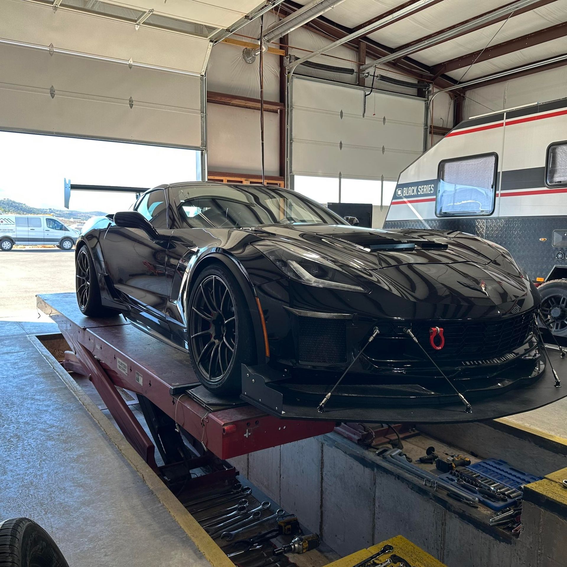 Black sports car on a lift in a garage, with front splitter and rear wing.
