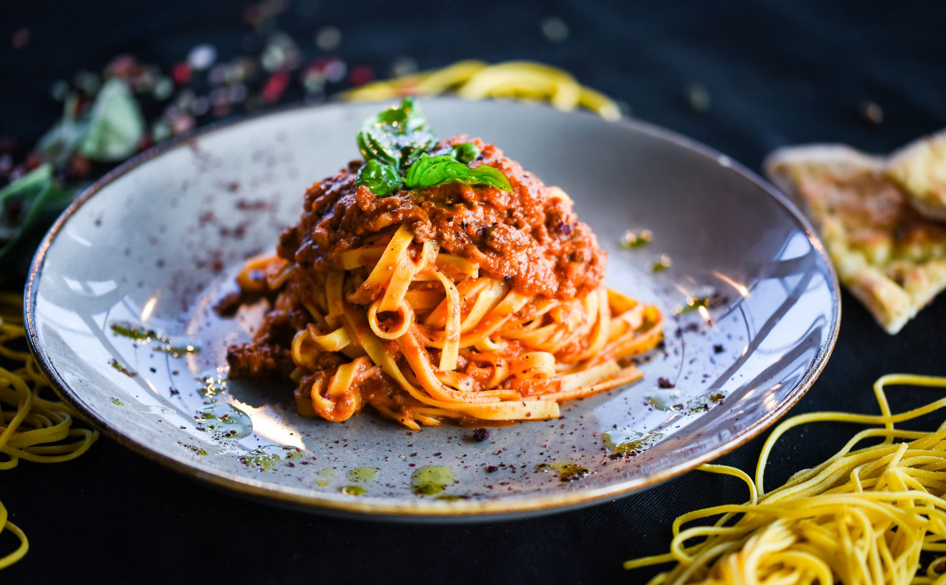 Pasta dish with meat sauce and basil garnish on a grey plate.