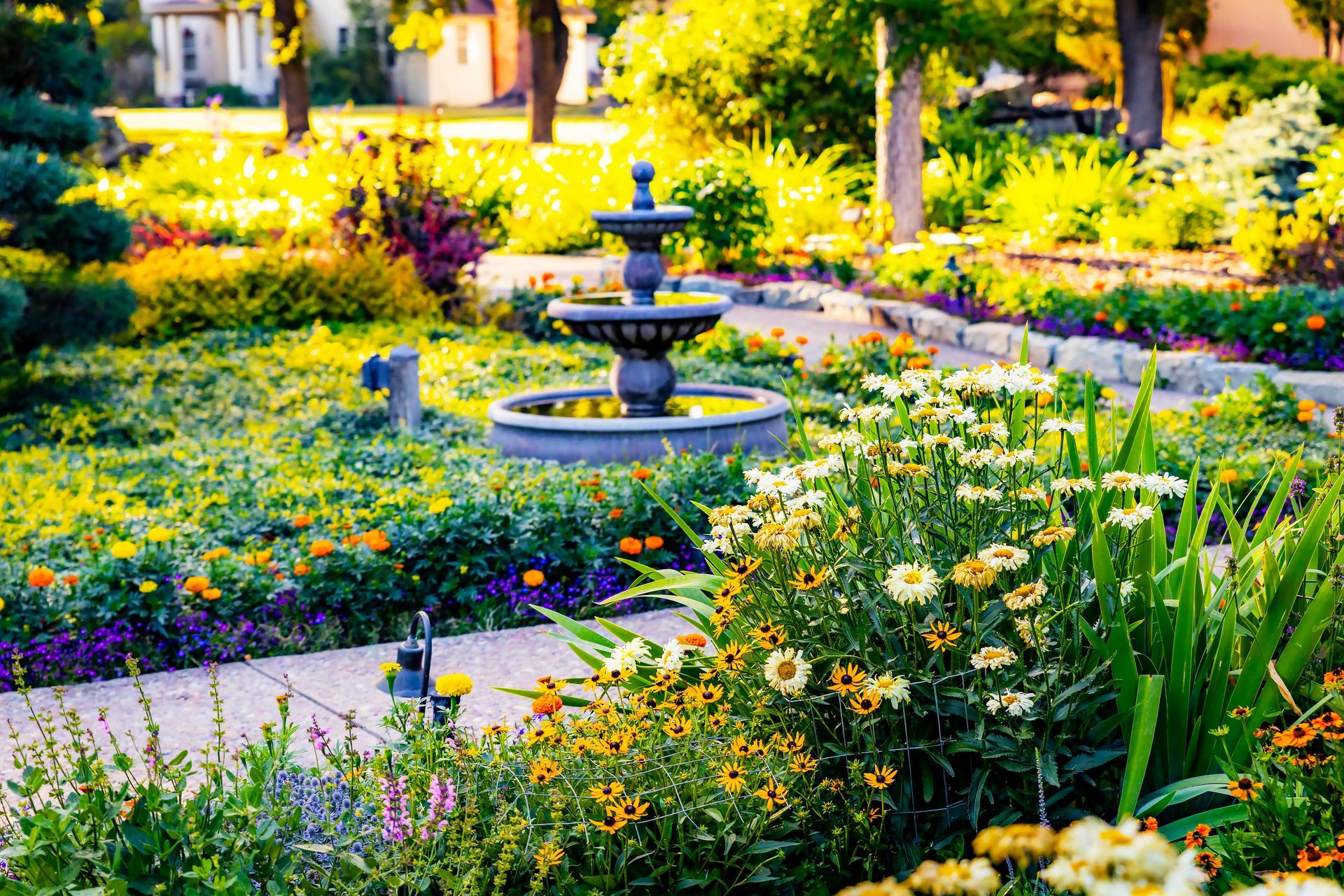 Lush garden with a tiered fountain, surrounded by colorful flowers and a pathway.