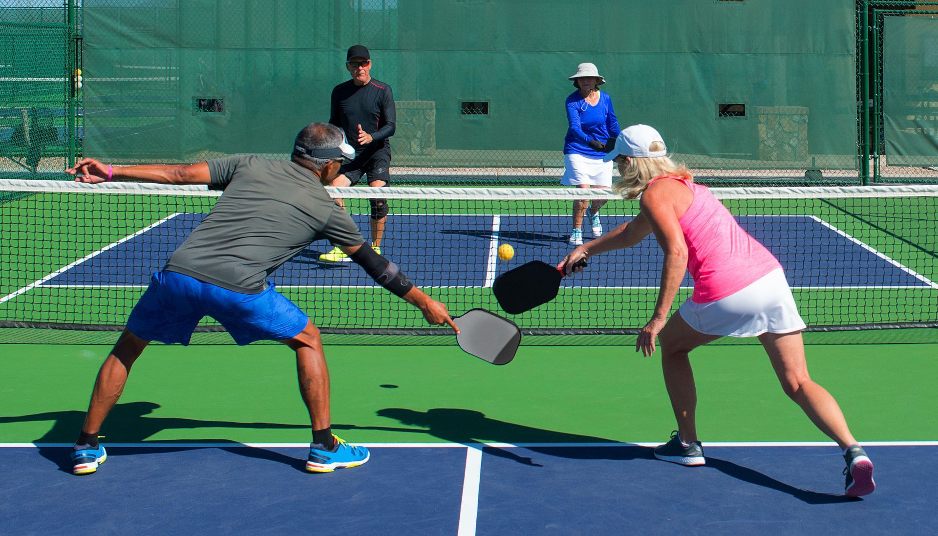 People playing pickleball on a court, man and woman facing each other near the net.
