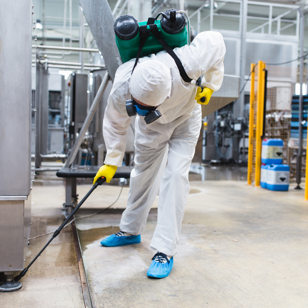 A man in a protective suit is using a sprayer in a factory.