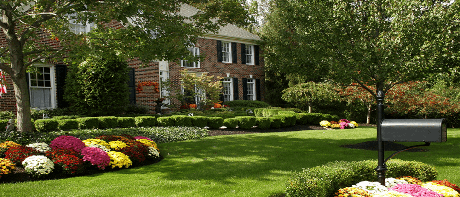 A lush green lawn with flowers and bushes in front of a brick house.