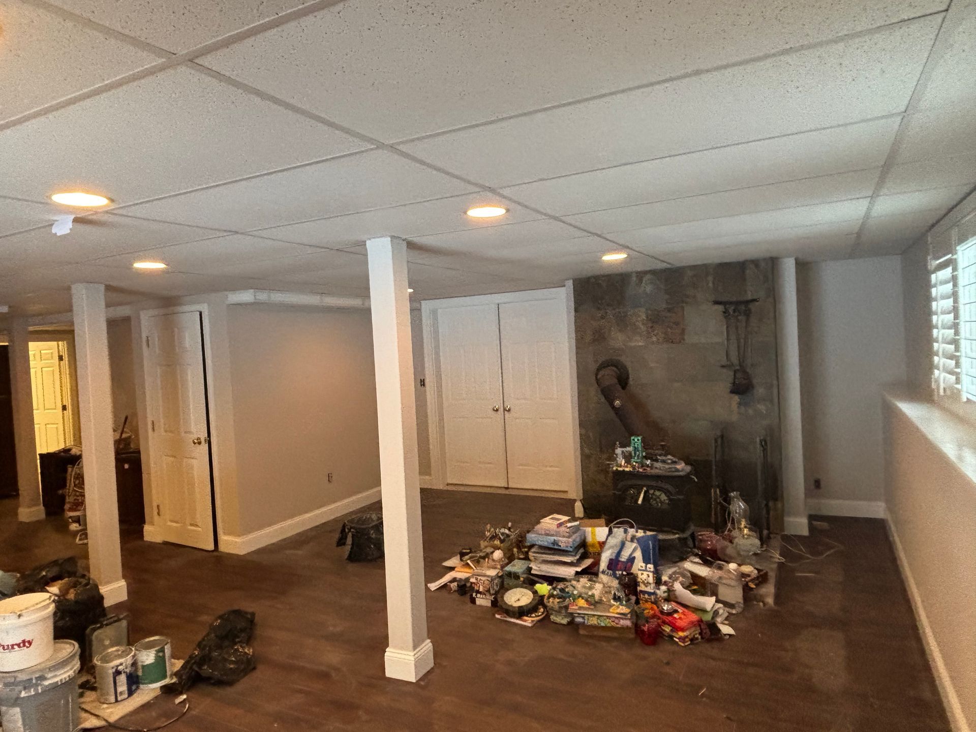 A partially finished basement with a stone fireplace, white columns, light-colored walls, and a pile of clutter on the floor.