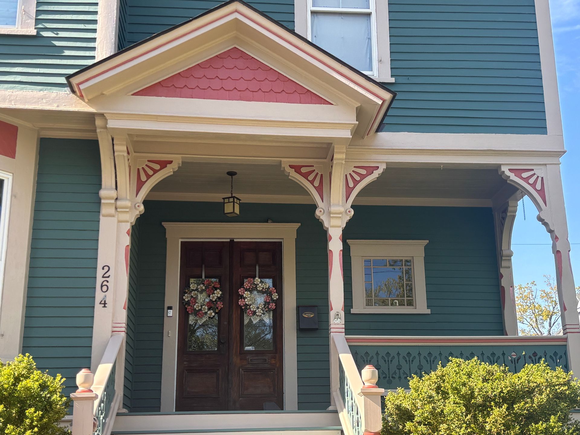 A teal-colored Victorian-style house entrance with a pink-accented porch, double wooden doors, and ornate trim.
