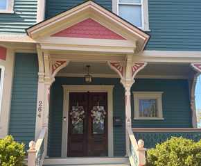 A teal Victorian home entrance with a decorative pediment, double dark wood doors with wreaths, and white trim.