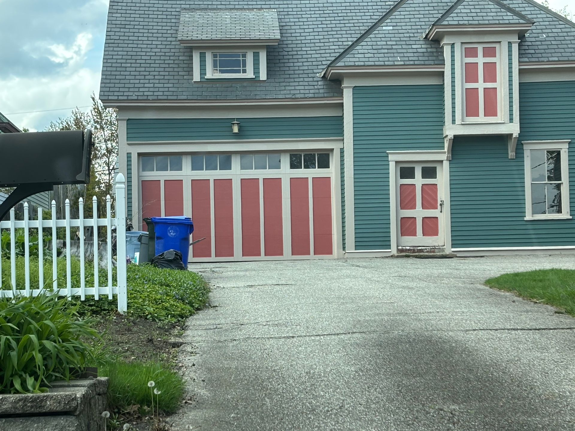A teal two-story house with a prominent garage door and matching door, both accented with salmon-pink panels.