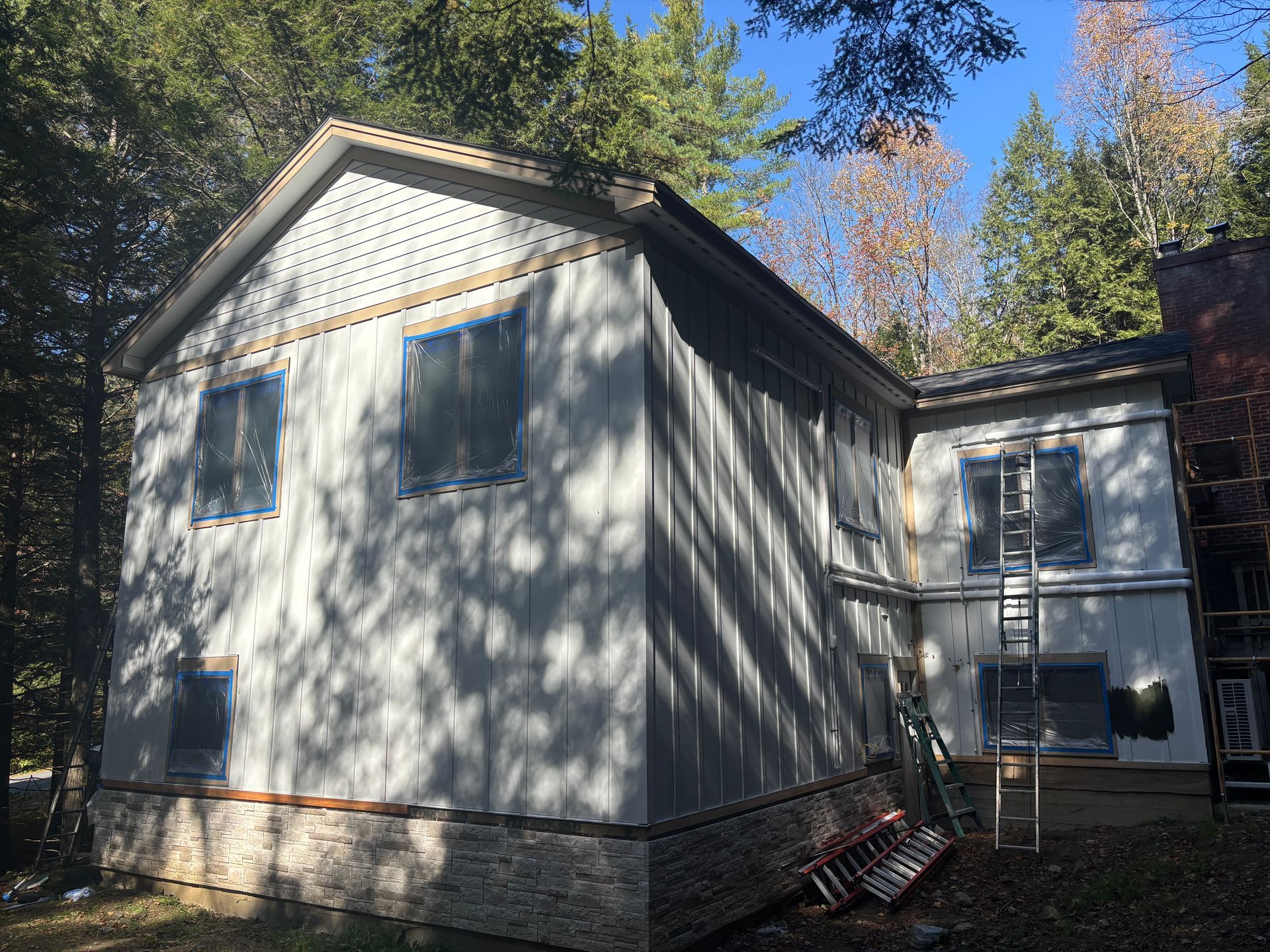 A two-story house under renovation, featuring exterior insulation panels, taped windows, and stone veneer foundation.