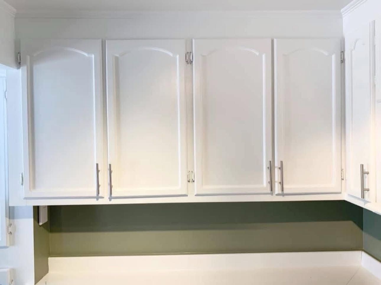 White kitchen cabinets with silver handles mounted above a green backsplash and a white countertop.