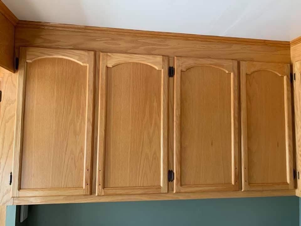 Four arched oak kitchen cabinets mounted against a white ceiling with a green wall beneath.